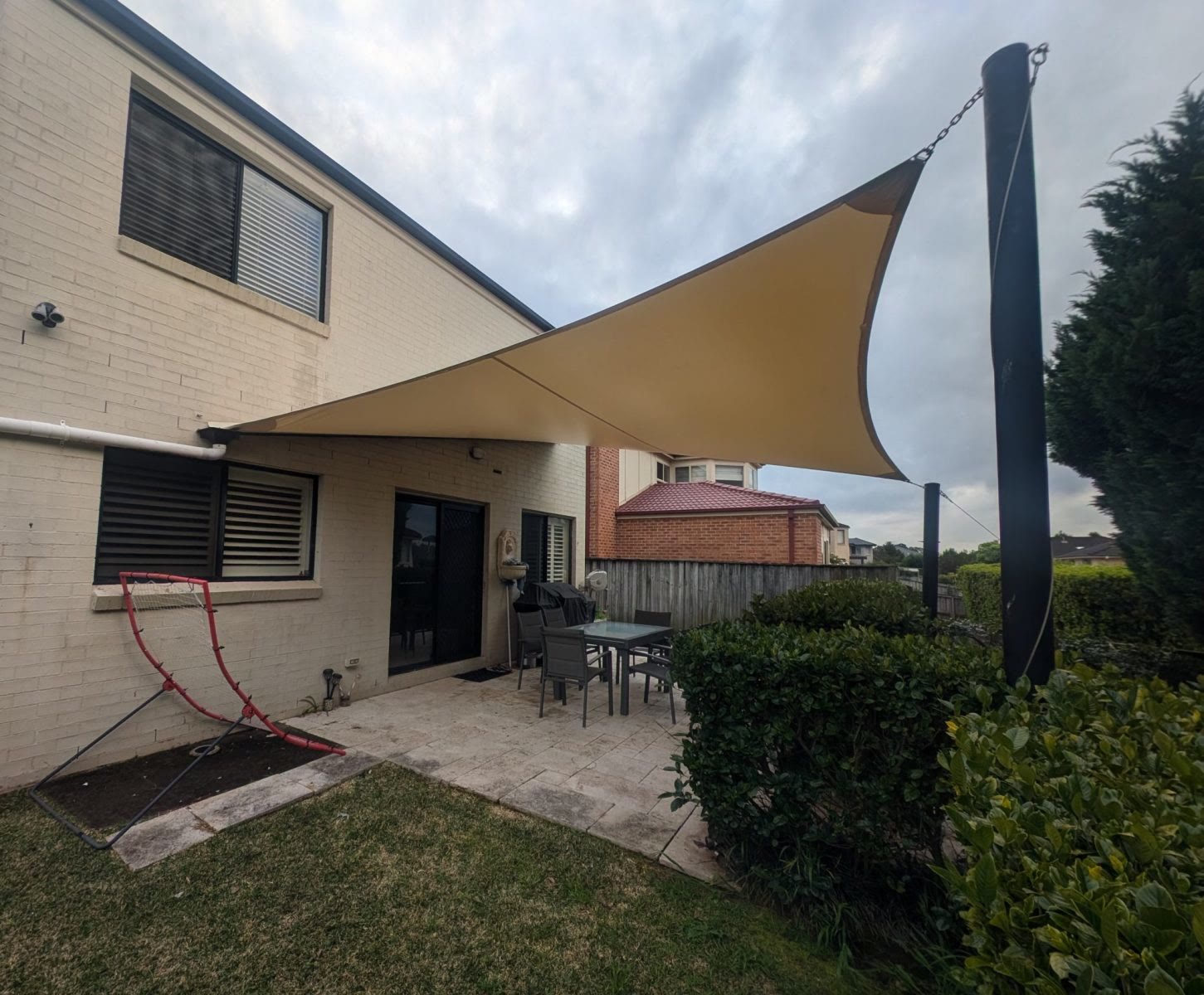 Sand-coloured shade sail stretched over a paved backyard patio and outdoor dining setting