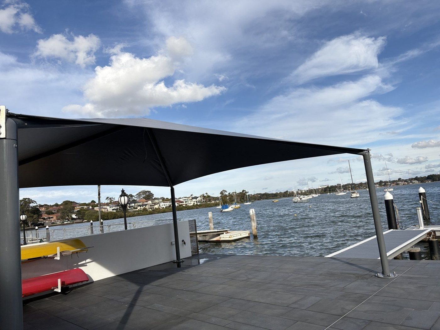 A charcoal canopy on steel posts shading a paved waterfront terrace