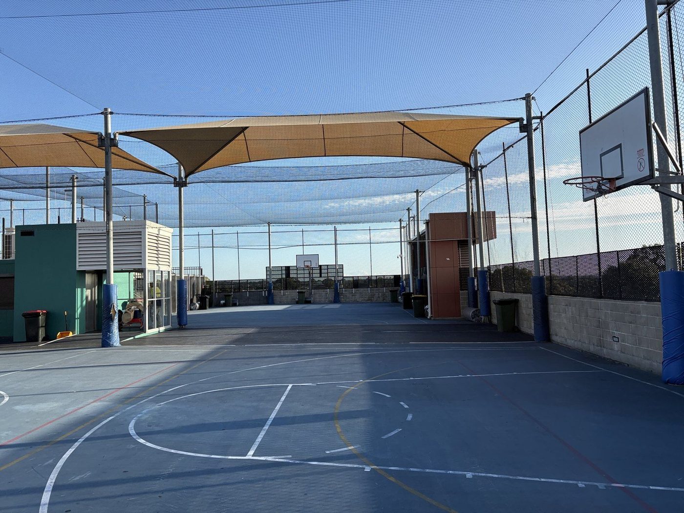 Sand shade sails stretched above a blue rooftop basketball court