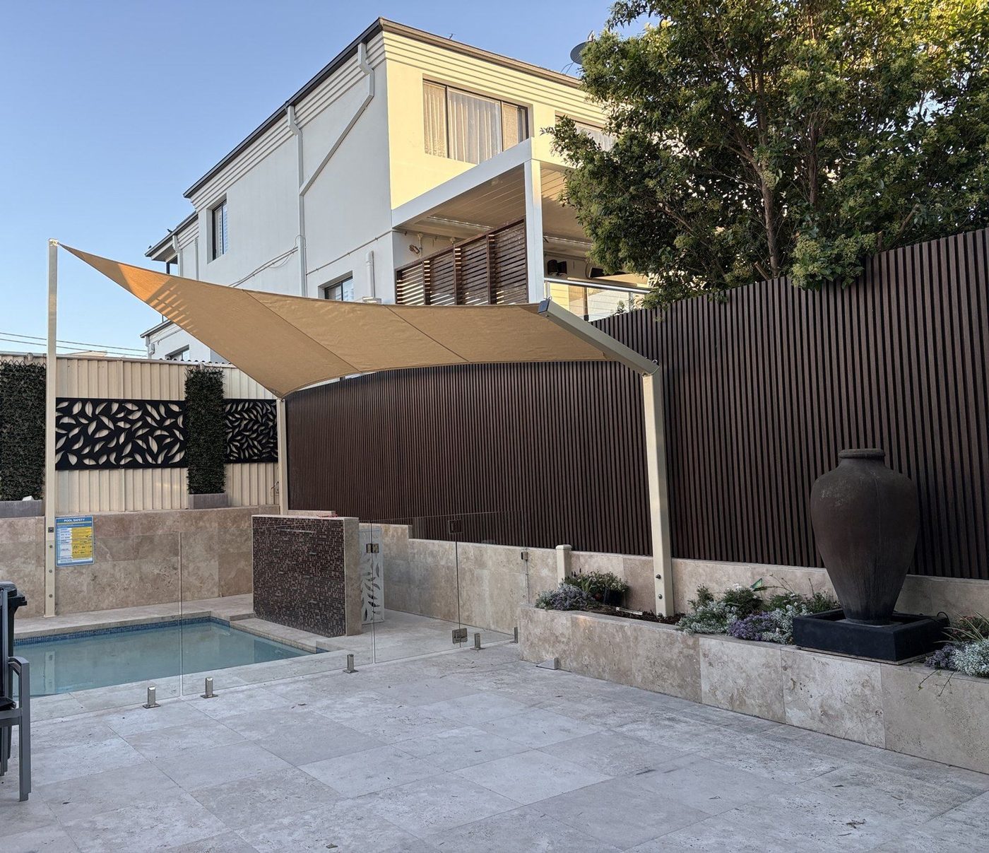 A sand-coloured shade sail on slim posts above a small courtyard pool