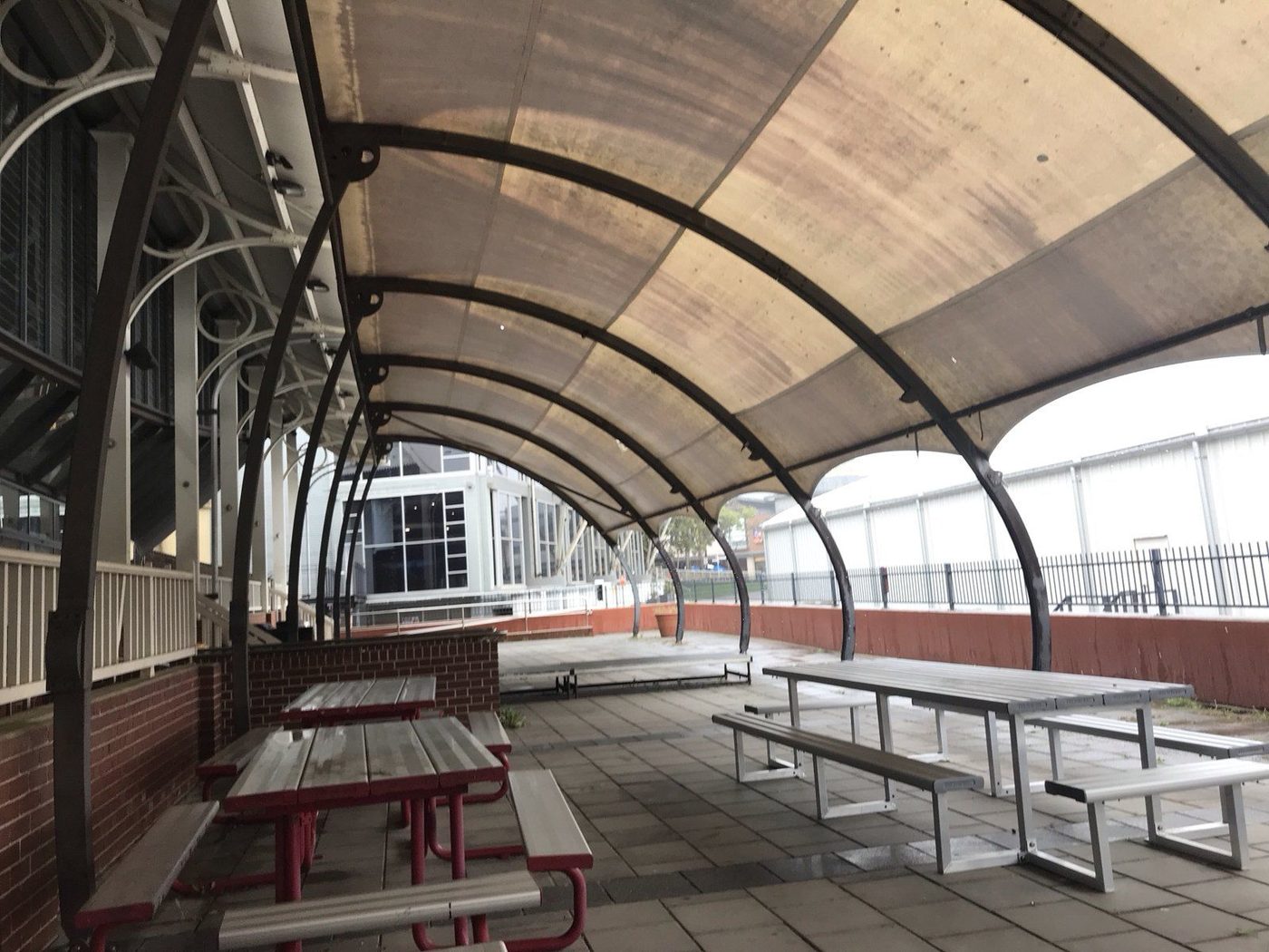 A curved barrel-vault canopy on black steel arches over public picnic tables