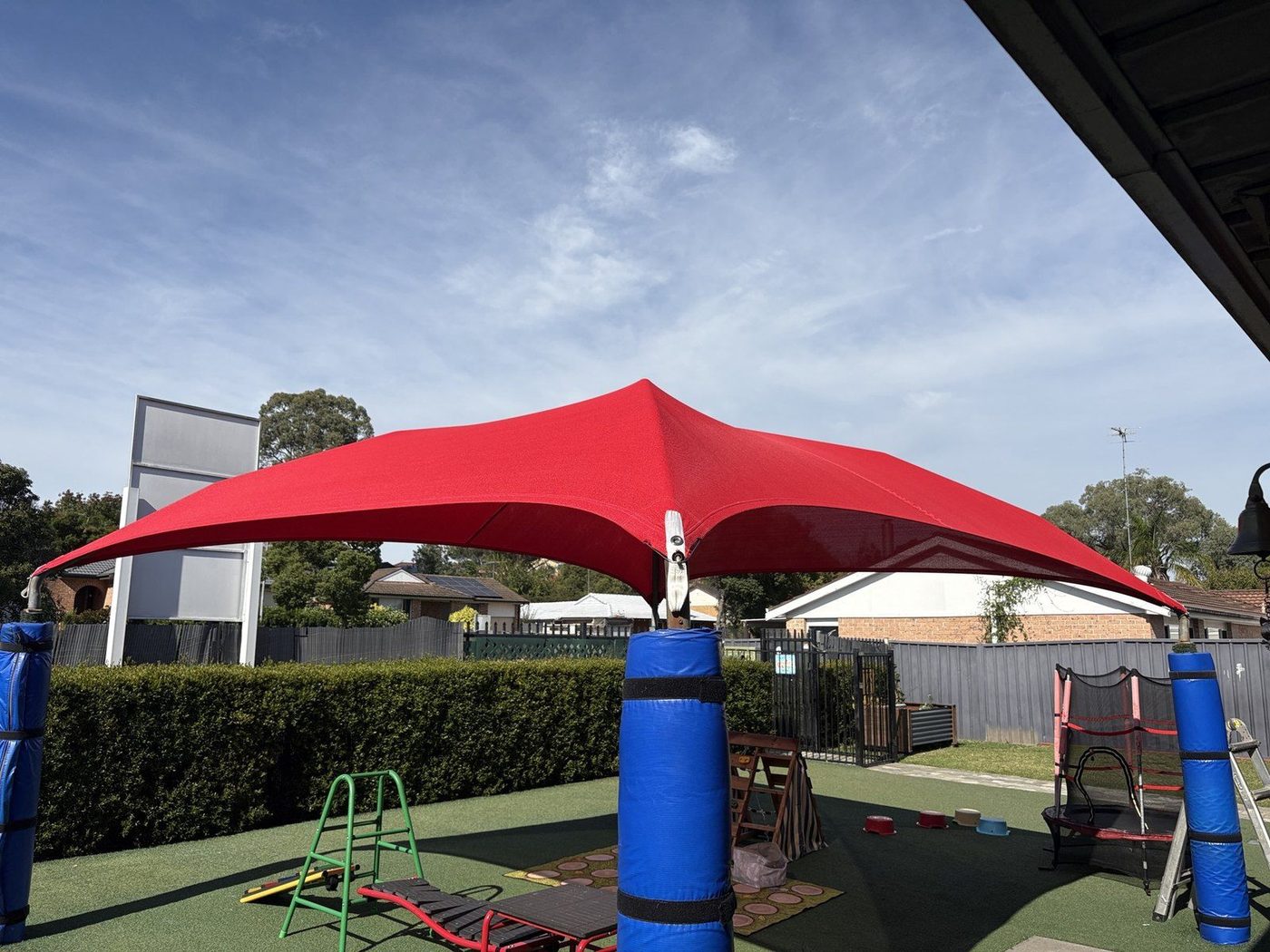 A red shade sail peaked on a central post above a play area