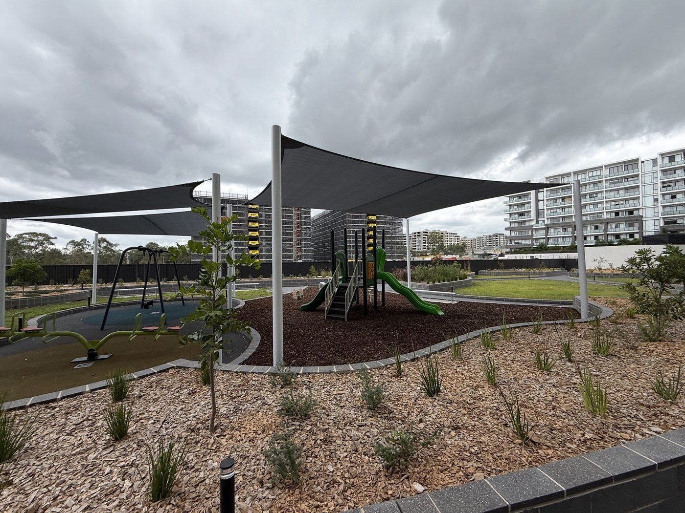 Charcoal shade sails on white posts above a playground in an apartment courtyard