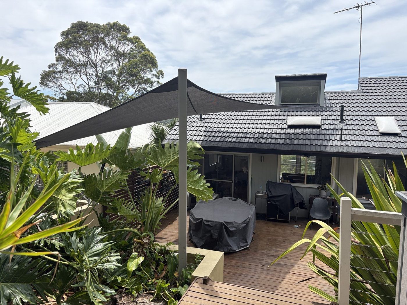 A charcoal shade sail on a steel post shading a timber deck beside a home