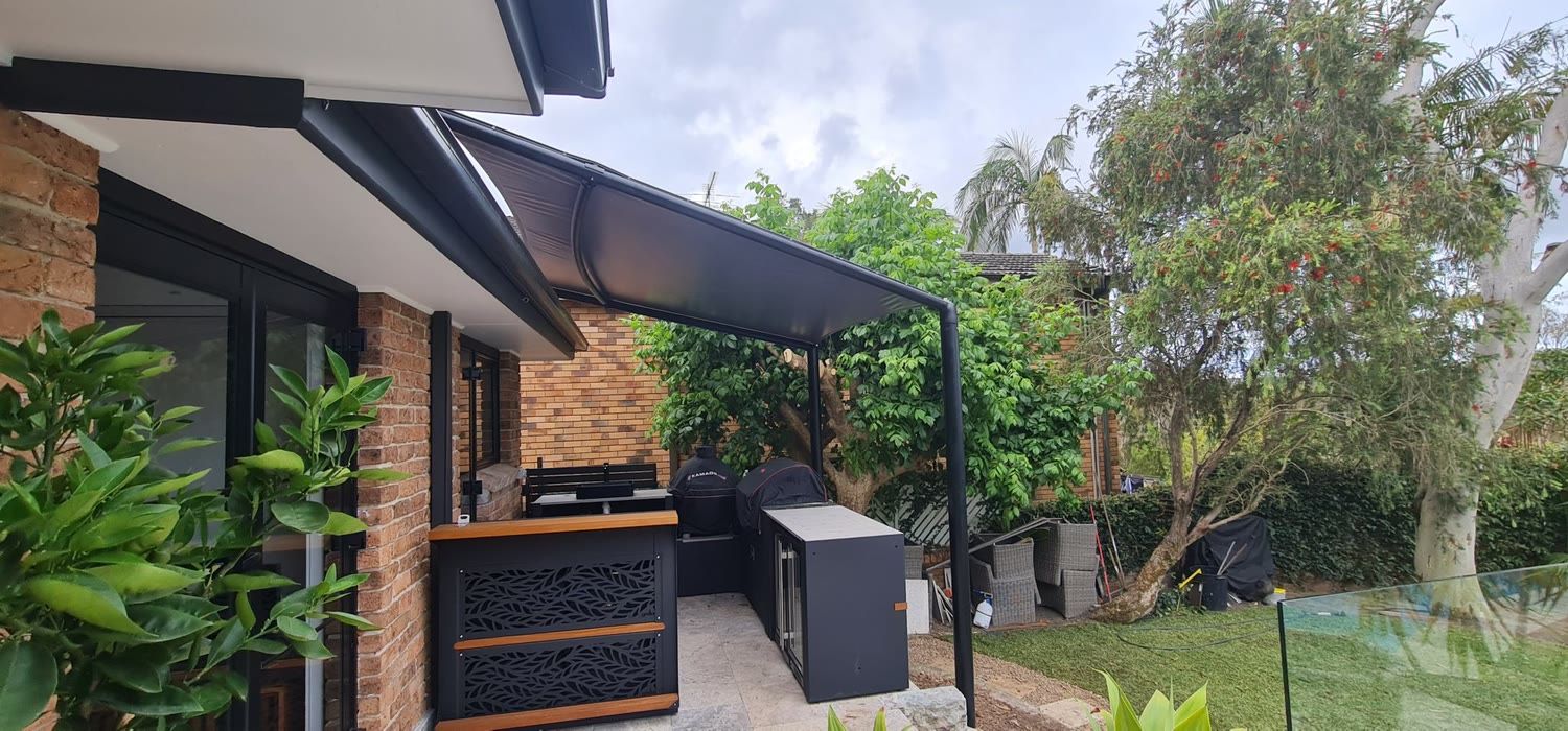 Dark waterproof canopy over an outdoor kitchen beside a brick home
